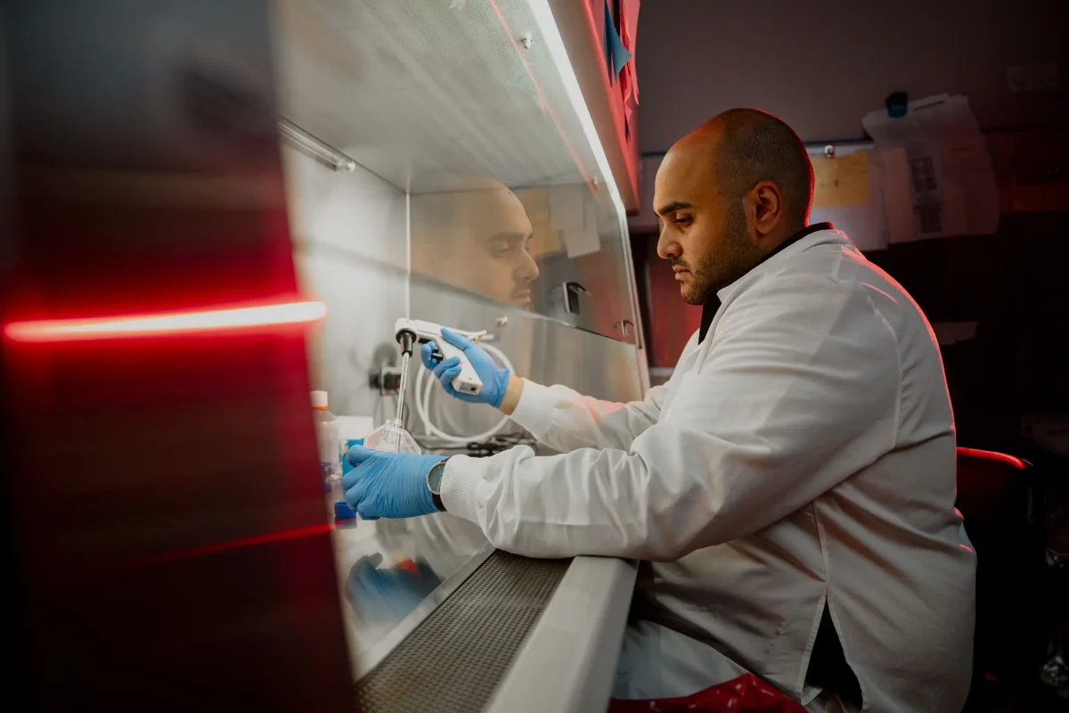 Laboratory researcher conducting sample preparation in a biosafety cabinet with a pipette