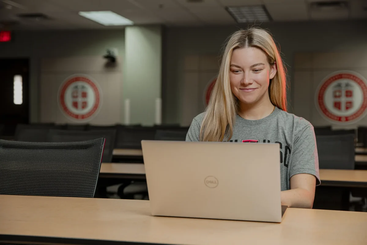 Person using a laptop at classroom desk with university logos in background